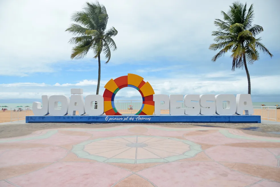 Letreiro turístico João Pessoa na orla da praia, com coqueiros ao fundo